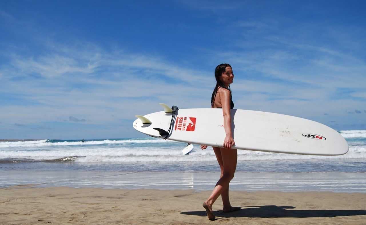 Surferka idzie plażą z deską w słoneczny dzień