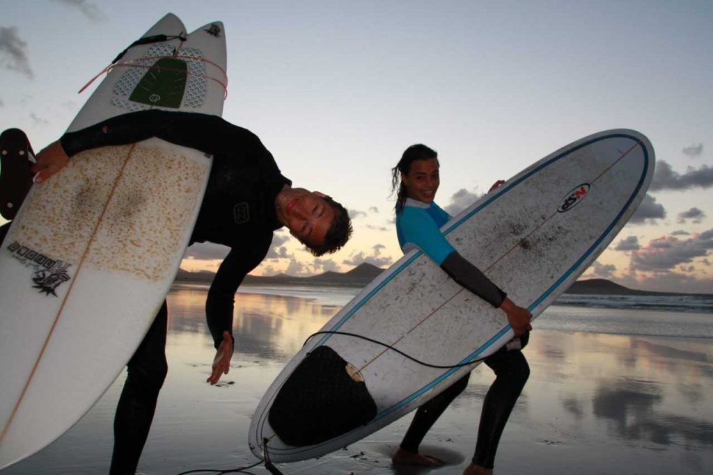 Surferzy niosą deski o zachodzie słońca w Famarze
