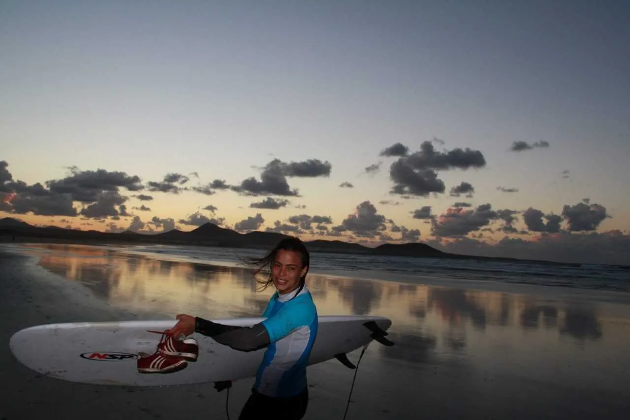 Surfer odbity w mokrym piasku o zachodzie słońca