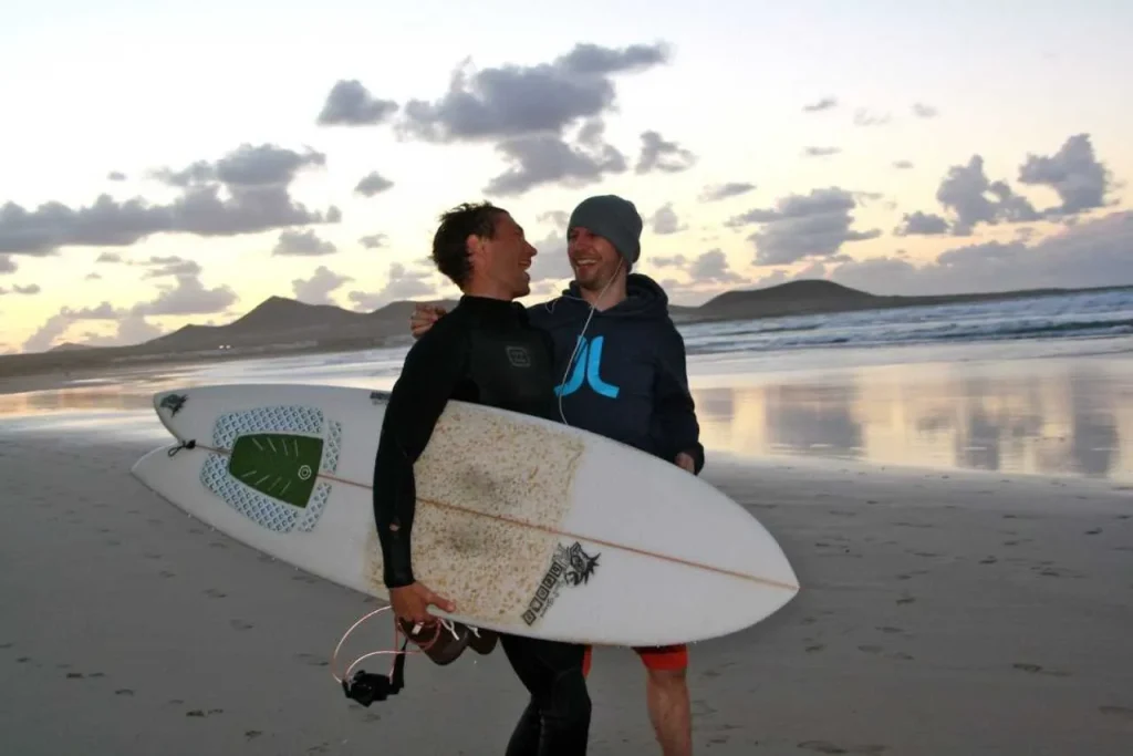 Dwóch surferów z deskami na plaży Famara o zachodzie słońca