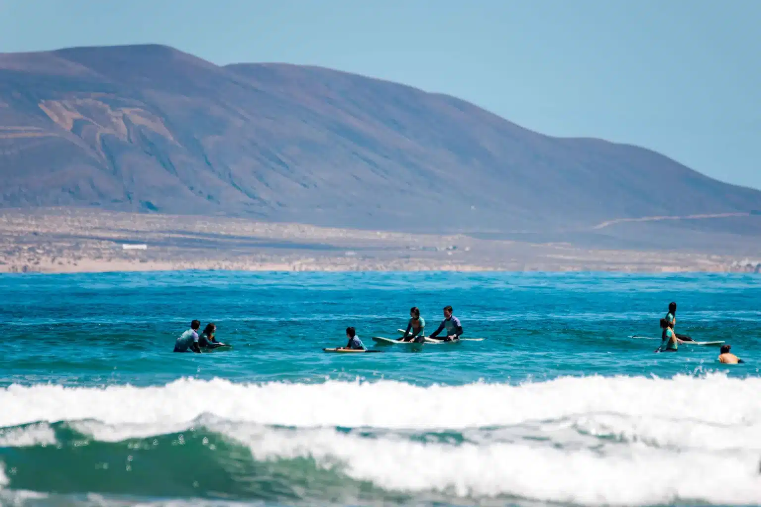 Surferzy na czystej fali na Playa de Famara z klifem Risco w tle