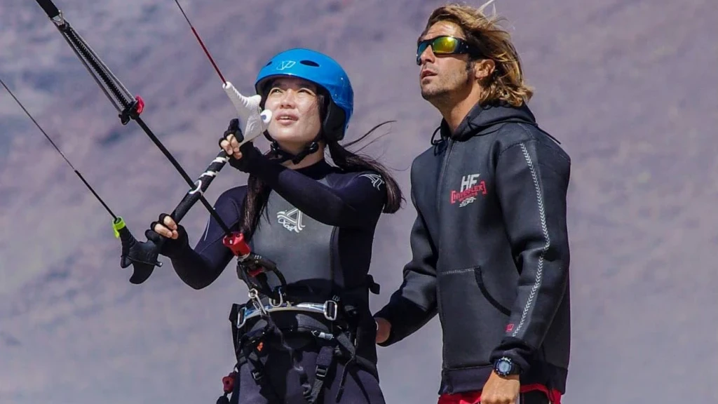 Lekcja kitesurfingu w Famarze: uczennica w kasku steruje latawcem, instruktor tuż obok