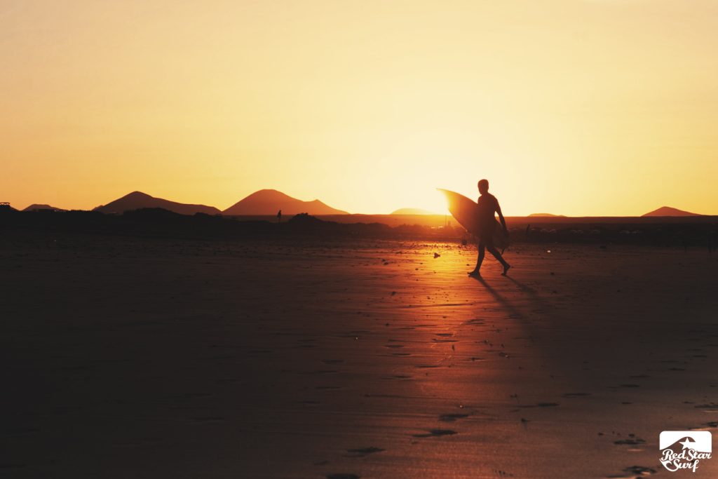 Surfer idzie plażą o zachodzie słońca w Famarze