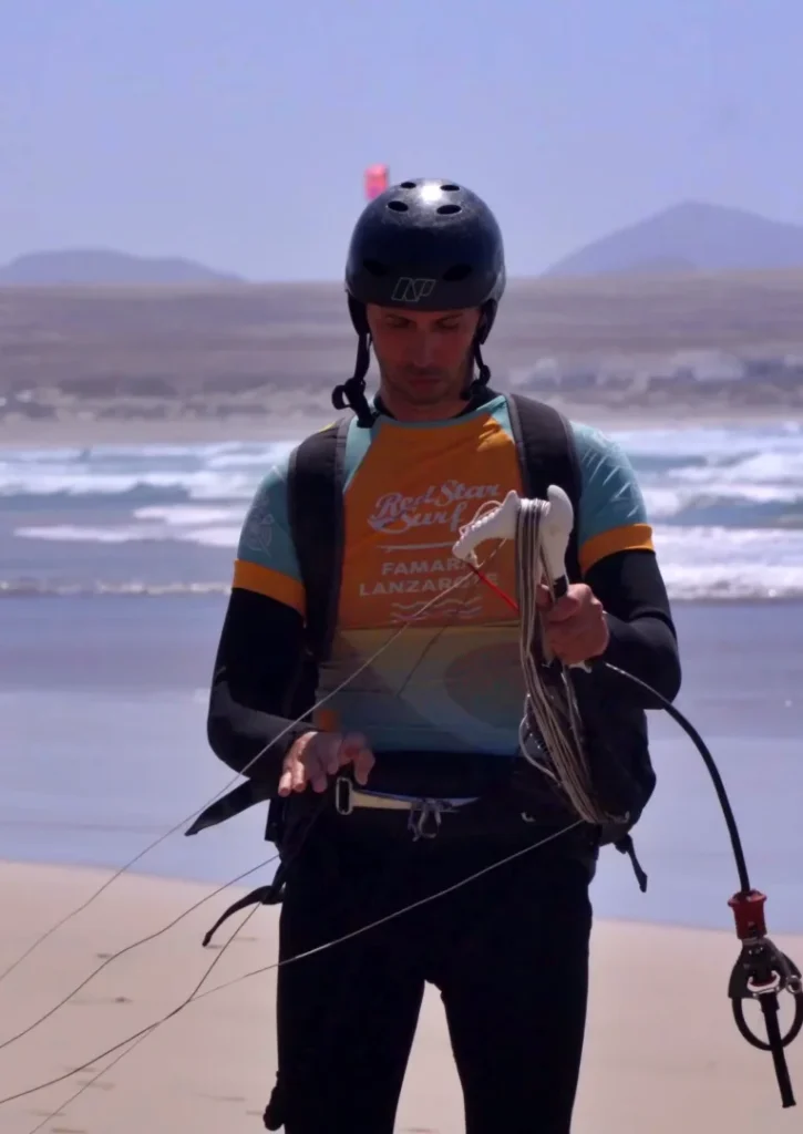 Allievo di kitesurf con il casco che tiene la barra sulla spiaggia di Famara, Lanzarote