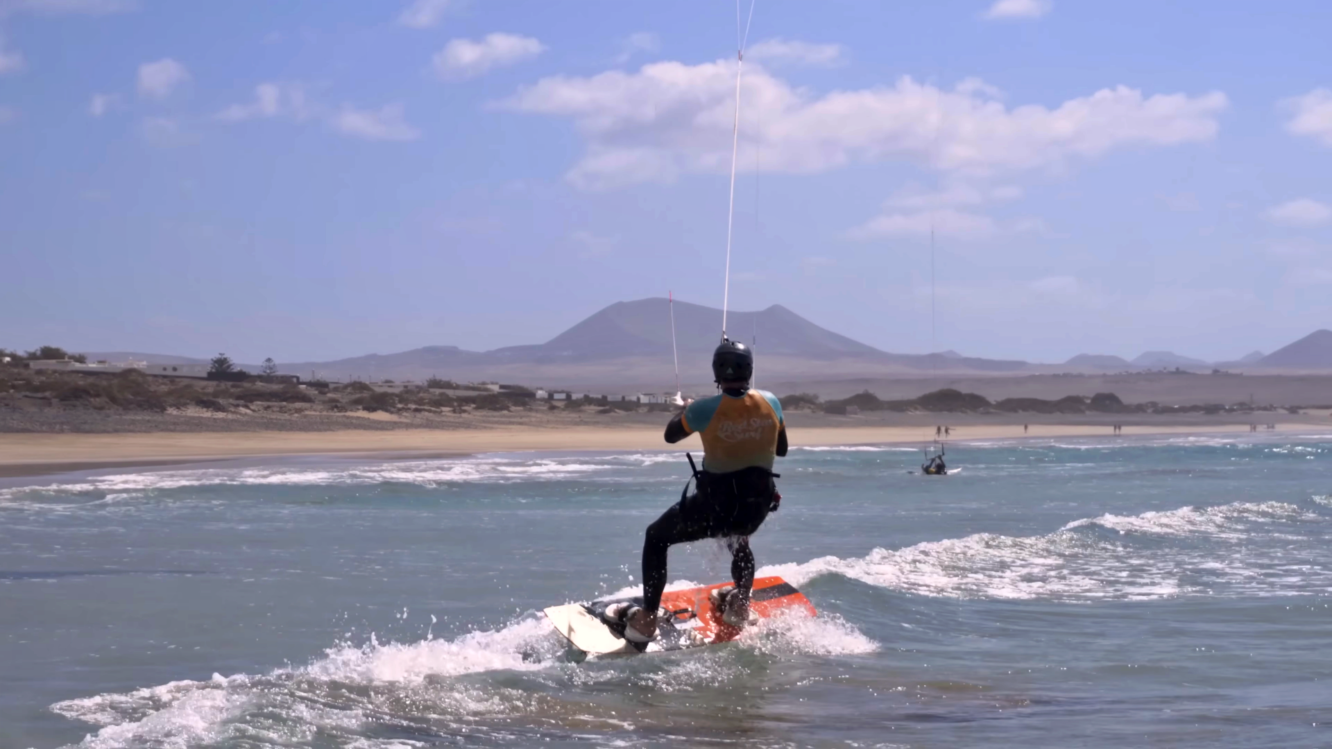 Allievo di kitesurf con il casco sulla tavola durante un water start a Famara, Lanzarote