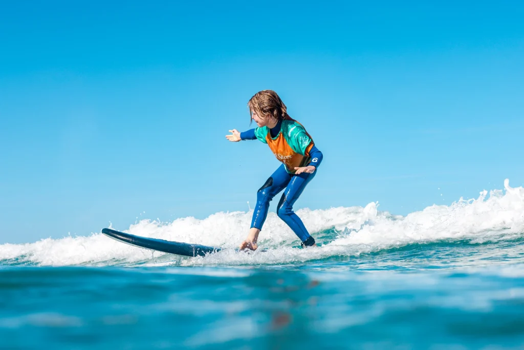 Child surfing a wave under a blue sky during a kids surf lesson in Famara, Lanzarote