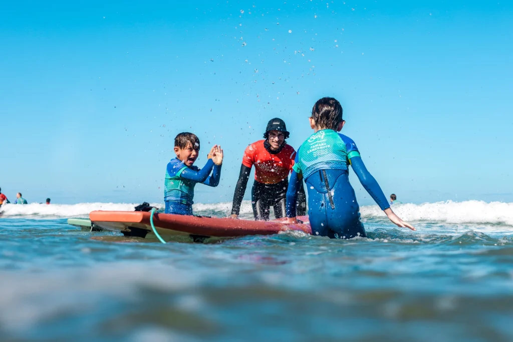 Two children high-fiving their surf instructor in the water during a kids surf lesson in Famara, Lanzarote