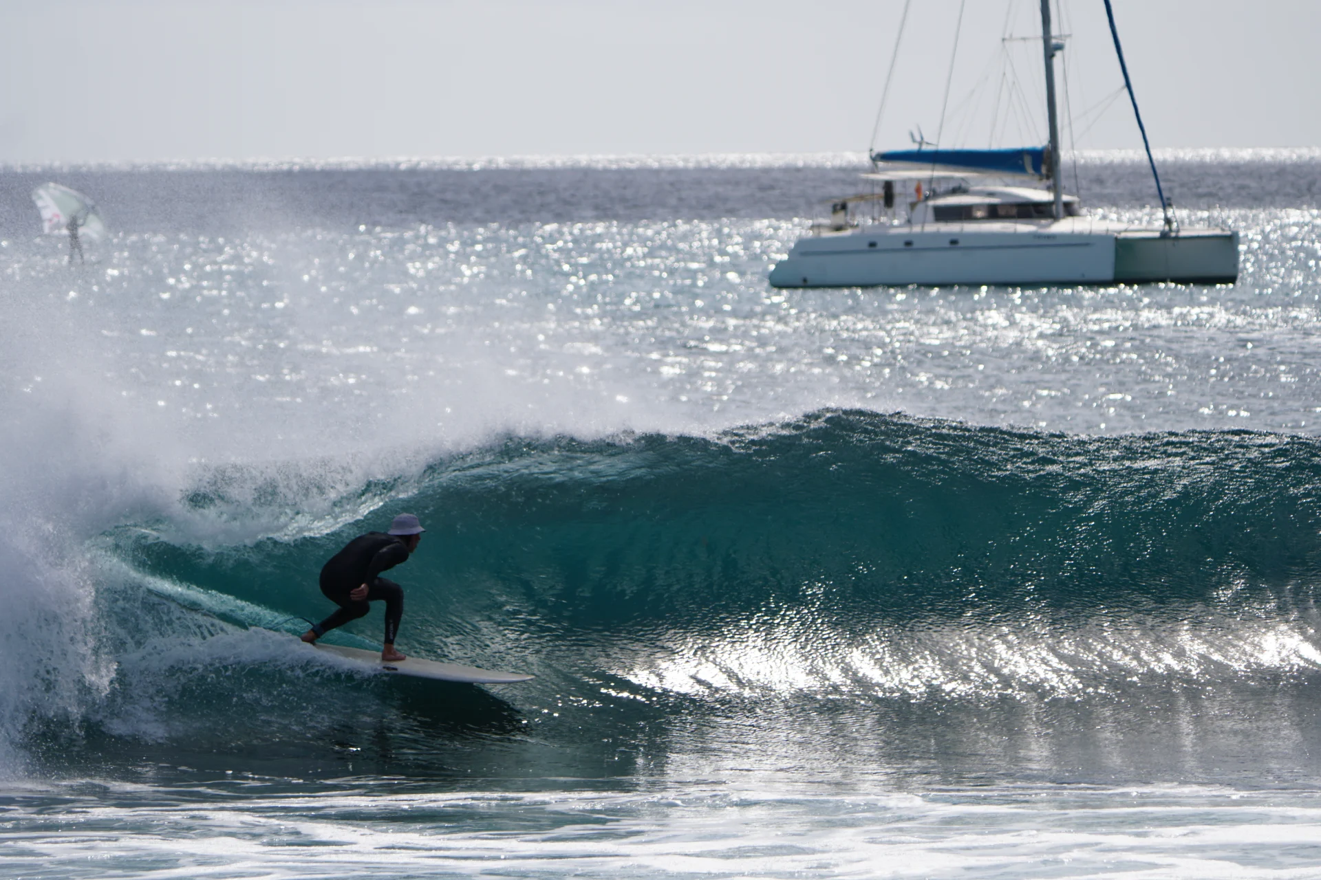 Surfista su un'onda di reef a Lanzarote con un catamarano all'ancora in controluce