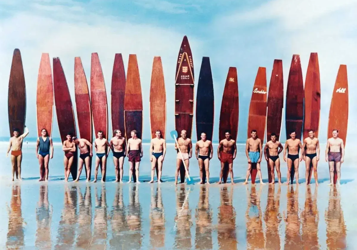 Line-up of solid wood surfboards from the 1930s, standing upright on the beach